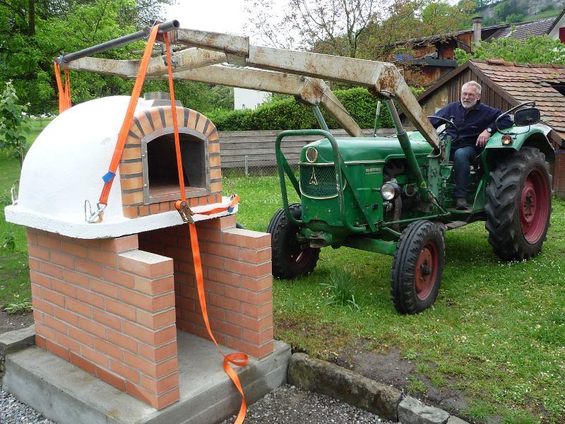 Ein Lisboa Holzbackofen wird mit einem Traktor und Frontlader auf ein Gestell gehoben