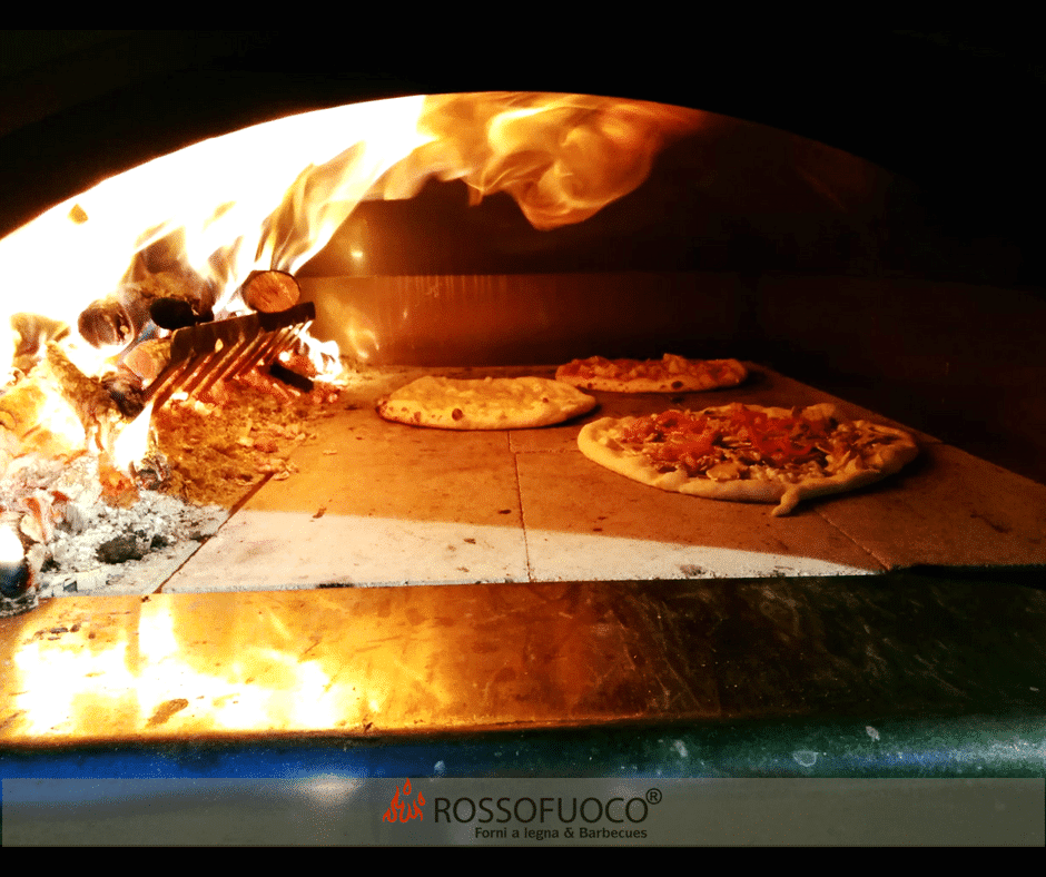 Ein Feuer brennt in einem Rosso Fuoco Pizzaofen in dem Pizzen gebacken werden