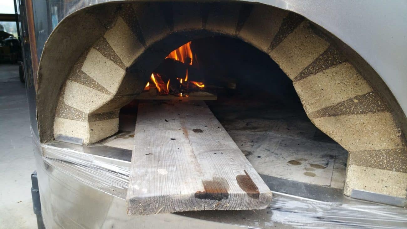 Pizzaofen trockenheizen Feuer mit einem Brett verteilen